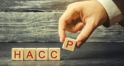 A man puts wooden blocks with the word HACCP. Hazard analysis and critical control points. Quality management rules for food industry. Food safety from biological, chemical, and physical hazards