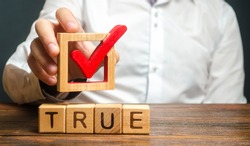 A man holds a red check mark over word True. Confirm the veracity and truth. Fight against fake news hostile propaganda. Confirmation facts, refutation of rumors. Debunking Myths and Misconceptions