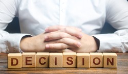 Man folded his hands on a background of blocks with the word Decision. Make the right decision, the answer to the question. Reasoning, weighing results and consequences. Authoritative opinion.