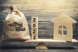 Money bag 2022 and a wooden house on the scales. Real estate concept. Family budget planning. Investments, plans, savings. Mortgage and mortgage rates. Forecasts. Loan. Refinance home