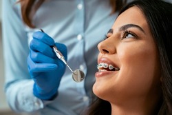 Beautiful girl with dental braces at dental checkup, smiling while dentist holding dental mirror