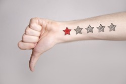 Man hand showing thumbs down and one star rating on the arm skin. Dislike