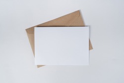 Blank white paper on the brown paper envelope. Mock-up of horizontal blank greeting card. Top view of Craft paper envelope on white background. Flat lay of stationery. Minimalism style.
