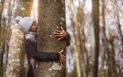middle-aged woman in white cap hugs and kisses a tree trunk. concept connection with nature. balneotherapy.