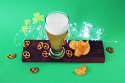 Patrick day, fresh foamy beer in a glass, chips and crackers on a wooden board, shamrock on a green background, party, congratulations, postcard
