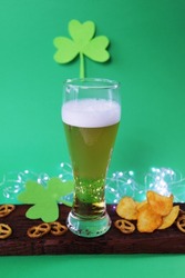 Patrick day, fresh foamy beer in a glass, chips and crackers on a wooden board, shamrock on a green background, party, congratulations, postcard