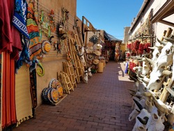 Colorful Spanish/Mexican, Southwestern Art and Textiles for Sale, Outdoors on a Side Alleyway, with Blue Skies and Bright Artwork on Both Sides of Alley; Travel, Tourism, Shopping