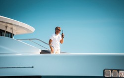 Male superyacht Deckhand with a handheld radio getting ready to drop anchor, with a blue sky in the background
