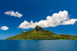 Seascape photo of remote island of Mangareva in the Gambier Archipelago of French Polynesia, South Pacific, blue sky and beautiful volcanic mountain covered in tropical vegetation