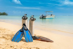 Scuba diving gear on display at pristine tropical beach diving holiday destination of Moorea, French Polynesia, with diving boat in the background, fins, dive tank and masks, sunny day blue skies