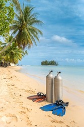Scuba diving gear on display at pristine tropical beach diving holiday destination of Moorea, French Polynesia, with diving fins, dive tank and masks, sunny day blue skies and palm trees