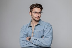 Fashionable young handsome model hipster man with vintage eyewear with hairstyle in blue denim shirt in studio on a gray background