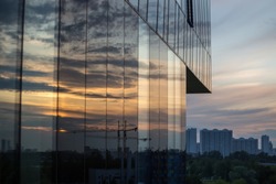 Modern office building with dramatic sunset sky and cityscape reflected on its glass wall.