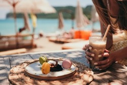 Woman hand holds Ice coffee latte on the beach. Summer iced coffee latte in tall glass with straw by the sea in beach bar coffee 