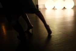 Detail of a couples feet dancing tango in a dark room, lit by three round lights