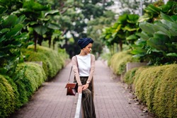 Portrait of a young Muslim woman in a hijab leaning on a railing in the park. She is wearing a blue turban and is elegantly dressed; she is of Arab, Malay, Asian descent and is attractive. 