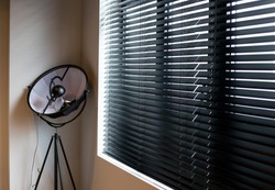Wood blinds black color closeup on the window in the interior. Wooden slats 50mm wide, black tapes. Venetian blinds closed in the room. There is a floor lamp near the window. 