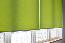 Roller blinds closeup on the window in the interior. Roller shades for big windows. Electric curtains for office. Green color, monochrome material. Window coverings.