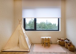 Roller blinds in the children's room. Automatic roller shades on the window in the interior of child's room. Trees outside. Electric sunscreen curtains for home. Playhouse and toys are there.