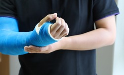 Closeup of asian man's arm with long arm plaster, fiberglass cast therapy cover by blue elastic bandage after sport accident. Appropriate treatment in western medicine.