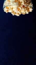 vertical image of a bowl of popcorn crashing down with navy blue background