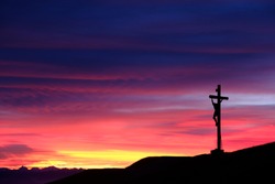 Sunset behind a mountain top cross in the Dolomites