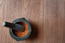Chili peppers in stone mortar on wooden background.