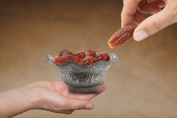 hand giving date fruit. Vintage metal bowl full of pitted date fruits on wooden table.  Traditional iftar food. Symbolizing Ramadan.