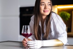 Happy girl with prosthetic arm holds glass of wine in artificial prosthetic limb hand at home