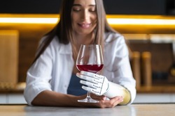 Calm thoughtful girl holds glass of wine in bionic arm at home, woman with artificial prosthetic limb