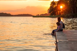 A woman and a little girl are sitting on the pier with their bare feet dangling in the lake. The union of mother and daughter. Idyll, calm, understanding, contemplation