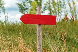Handmade wooden direction sign in countryside meadow with blank signage as copy space pointing to the left, selective focus