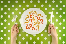 Woman eating question marks on a white plate, top view above polka dotted table cloth. Unknown or unrecognizable food concept.