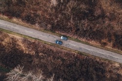 Top view drone photography of car overtaking the parked automobile along the road through wooded landscape in autumn afternoon, vehicle insurance concept