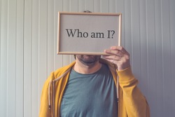 Introspective man  - Who am I, self-knowledge concept with question covering adult male face.
