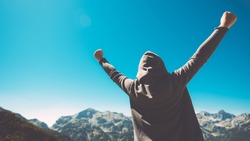 Winning and success. Victorious female person standing on mountain top with arms raised in V. Achievement and accomplishment in life. Toned image.