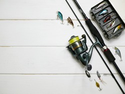 Fishing tackles lay on white wooden boards. Set of fishing tackles. Top view on spool, rod, spoons, wobblers and lure box.