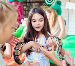 A beautiful girl is holding a python snake on her hands.