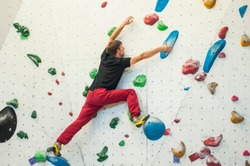 Climber in a boulder gym. Man climbing bouldering problem. Colorful volumes and holds on a white wall.