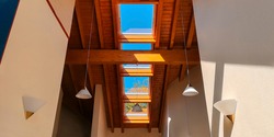 View of ceiling of gable roof without attic with three plastic windows, finished with clapboard,wooden beam,identical suspended white frosted lamps,2 symmetrically on white walls.Selective focus.