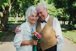 Old couple is walking in the green park. Grandmother and grandfather at their golden wedding anniversary celebration. Fifty years together love story of elderly people. Grandma and grandpa laughing.