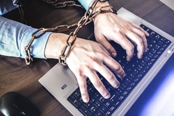 Man's hands in old rusty chains. In the trap of office work. Routine job. Manager near the laptop.