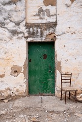 A dilapidated house with a green door and an old chair next to it