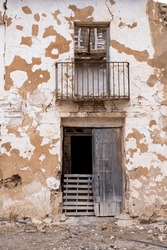 A dilapidated house with a barricaded door and a balcony, the plaster is crumbling from the facade