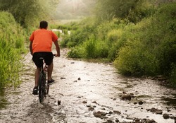 boy with orange shirt during a cycling adventure along a creek. Flare and light effect, scenic shot. Low point of view. Ideal for concept of fredoom, happiness and adventure. Splash of water
