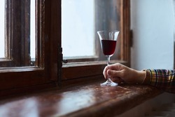 A young man drinks red wine from a vintage glass in an old mansion. Front view.