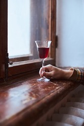 A young man drinks red wine from a vintage glass in an old mansion. Vertical photo.