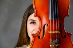 Concept musician violinist. Portrait of a pretty brunette girl in a white sweater playing the violin on a gray background