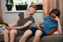 Photo of ordinary family relationships. Mom and teen look at the phone of their son at home while sitting on the sofa