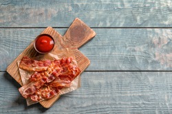 Board with fried bacon and sauce on wooden background